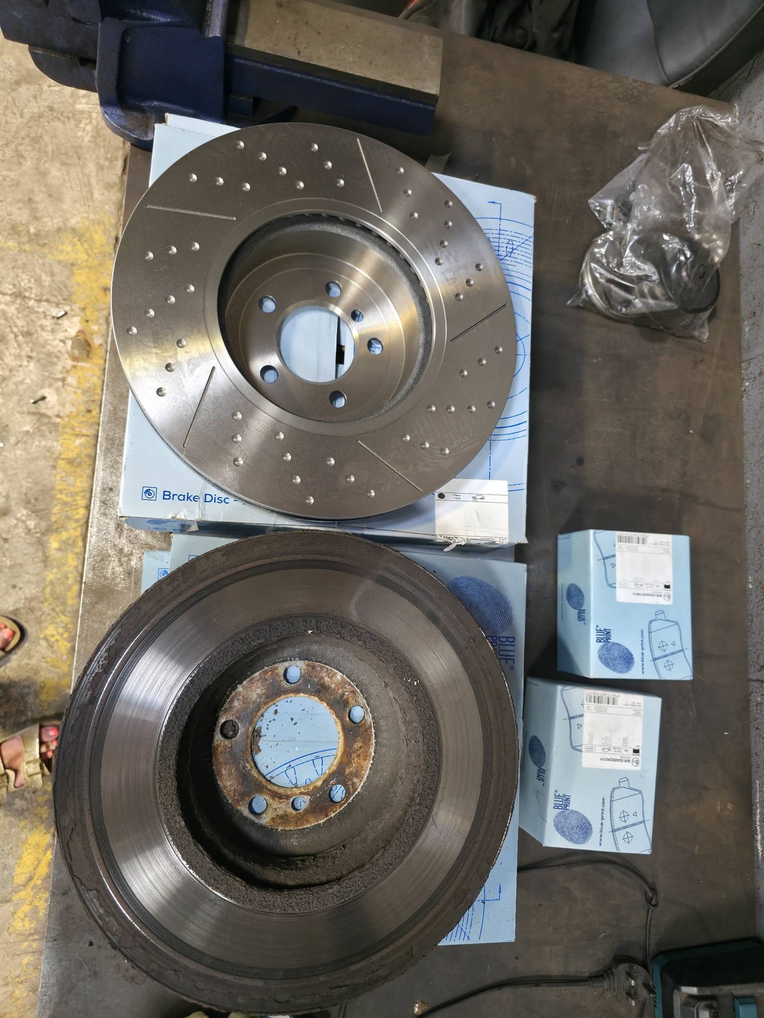 New drilled and grooved brake discs and pads laid out on the bench next to the worn discs they replaced