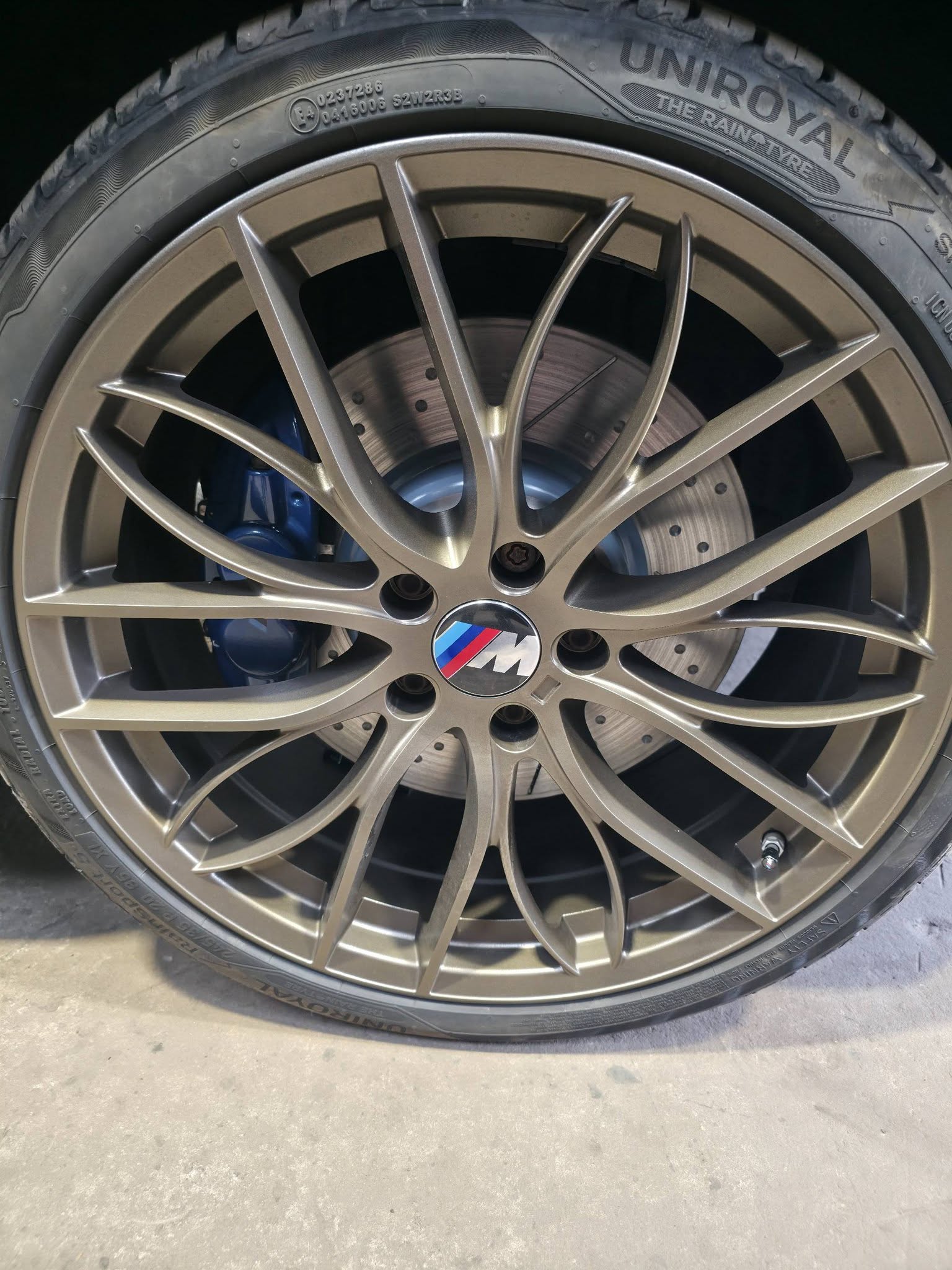 A BMW M alloy wheel with drilled brake discs and a blue caliper behind the spokes
