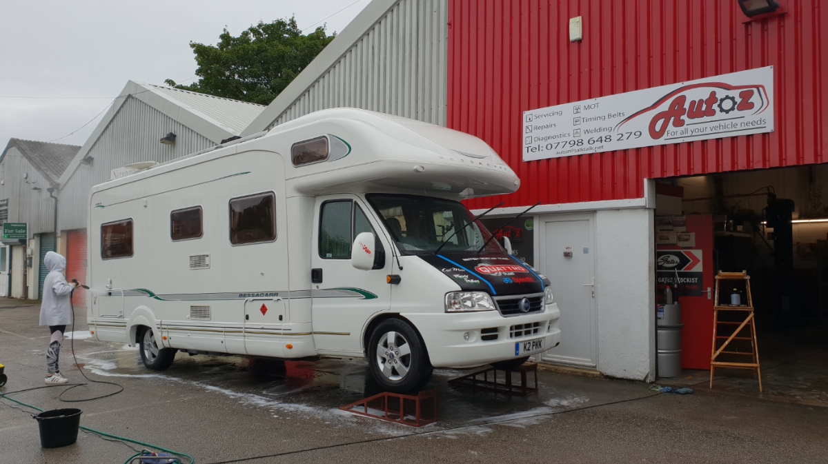 A motorhome on axle stands being worked on outside the red Autoz workshop