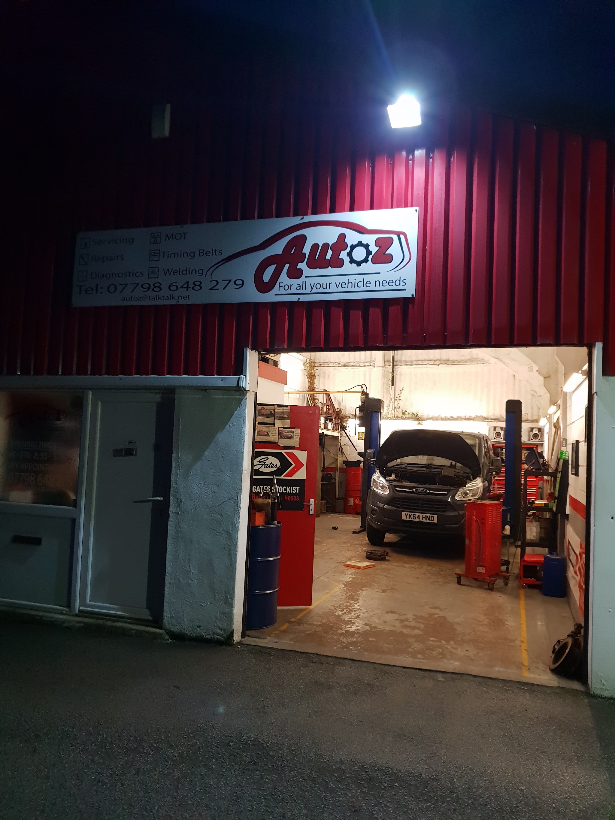 The Autoz workshop after dark with the sign lit and a vehicle up on the ramp inside the open door