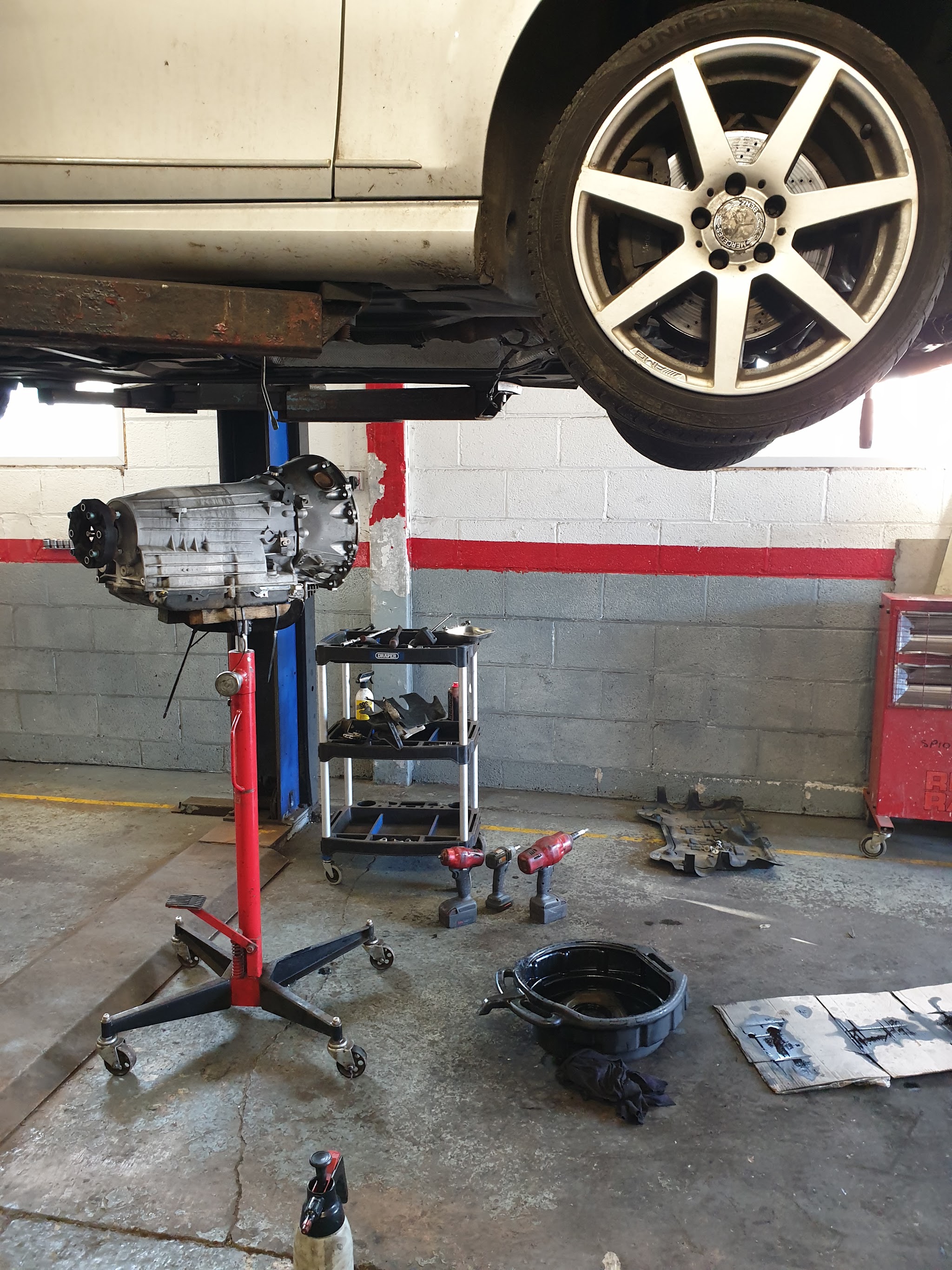A car raised on the lift with its gearbox lowered on a transmission jack underneath