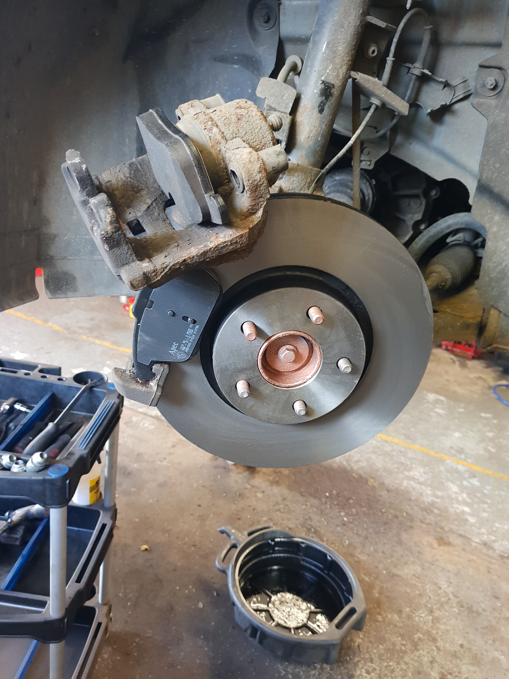 A new brake disc fitted to a car's hub with the caliper hanging beside it